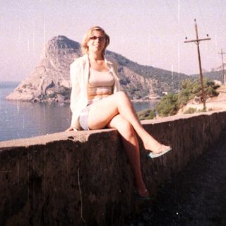 Woman sits on wall overlooking a coastal landscape.
