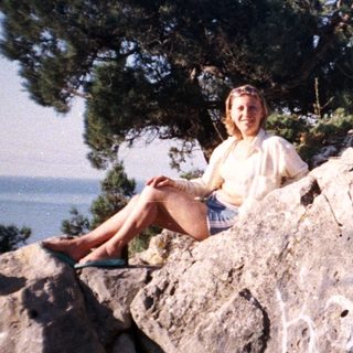 Woman sits on a rocky outcrop overlooking a sea view.