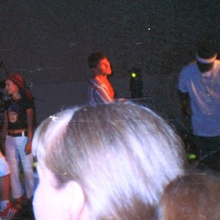 Group of people on stage, possibly performing, under spotlights.