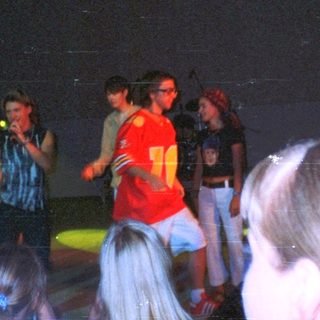 Group of people on stage, possibly performing, under spotlights.