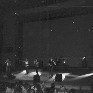 Concert performers on stage with stage lights and audience.