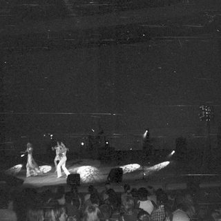 Performers on stage with audience visible in the background.
