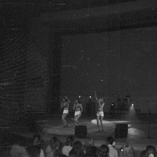 Three dancers perform on stage with blue lighting.