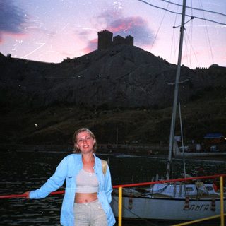 Woman stands near a boat with a castle in background.