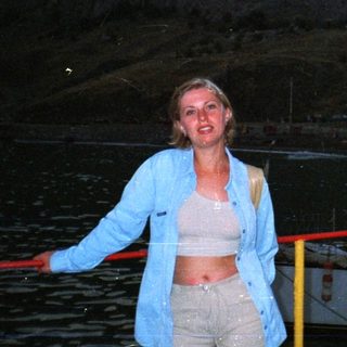 Woman stands near a boat with a castle in background.
