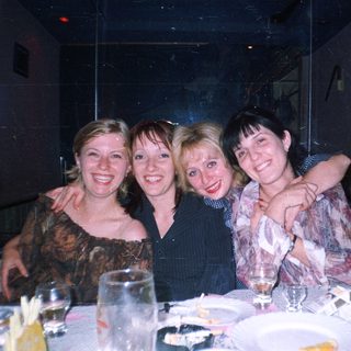 Four smiling women are grouped at a table.