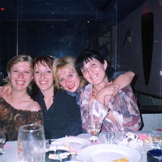 Four smiling women are grouped at a table.