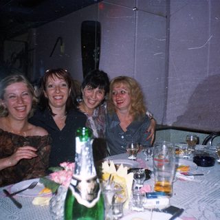 Four women are posing at a table with drinks.