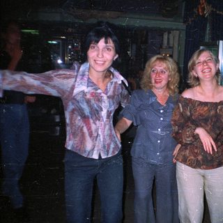 Three women stand smiling in an indoor setting.