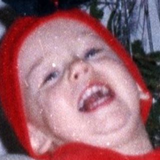 Child in festive clothing stands near a decorated Christmas tree.