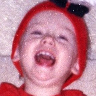 Infant wearing a red hat and outfit sits on a couch.