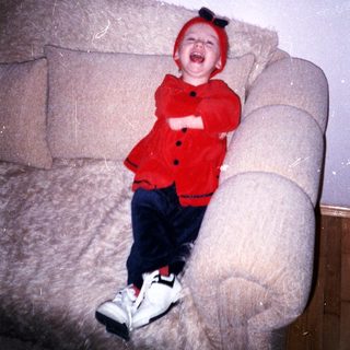 Infant wearing a red hat and outfit sits on a couch.