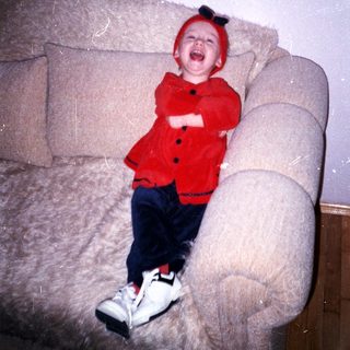 Infant wearing a red hat and outfit sits on a couch.