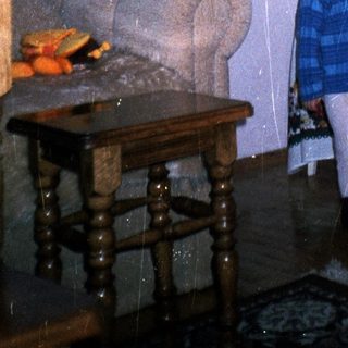 Child stands beneath a small, decorated Christmas tree.