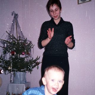Boy running toward a woman near a small Christmas tree.