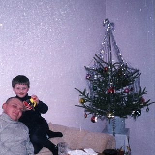 Man and child relax near a table with food and Christmas tree.