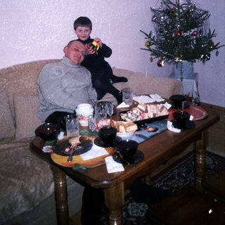 Man and child relax near a table with food and Christmas tree.