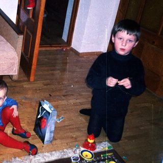 Two young boys play with toys on a rug.