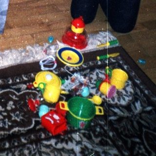 Two young boys play with toys on a rug.