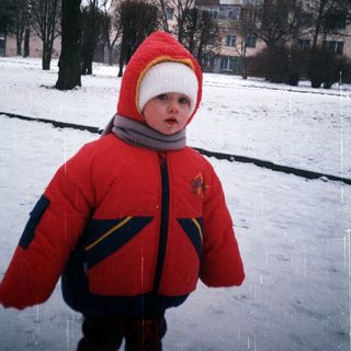 Child in winter coat stands in snowy landscape.