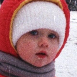 Child in winter coat stands in snowy landscape.