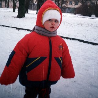 Child in winter coat stands in snowy landscape.