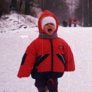 Child runs through snowy park on a rainy day.