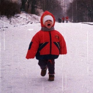 Child runs through snowy park on a rainy day.