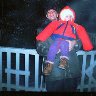 Man holds child, possibly ice skating, at night.