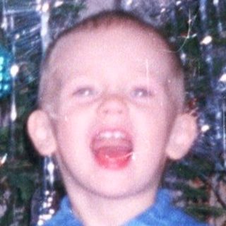 Child stands near a Christmas tree with tinsel.