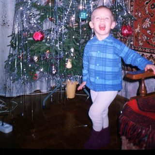 Child stands near a Christmas tree with tinsel.