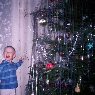 Boy stands near Christmas tree with mouth open.