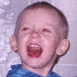 Boy stands near Christmas tree with mouth open.