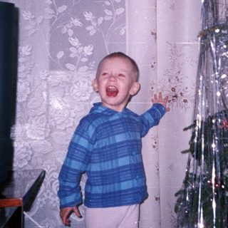 Boy stands near Christmas tree with mouth open.