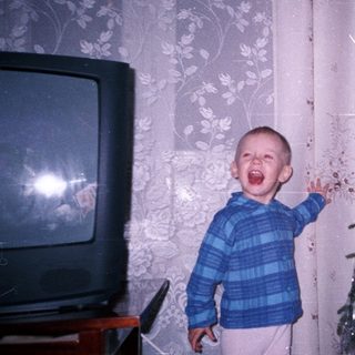 Boy stands near Christmas tree with mouth open.