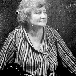 Here's a brief summary of the image: Older woman sits with a slight smile, wearing a striped shirt.