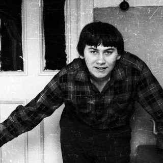 Man in plaid shirt stands near a door.