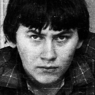 Man in plaid shirt stands near a door, looking forward.