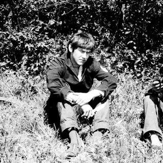 Two boys sit in tall grass, appearing thoughtful.
