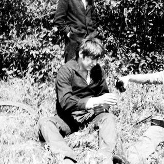 Here's a brief summary of the image: Three people sitting in tall grass near a bicycle.