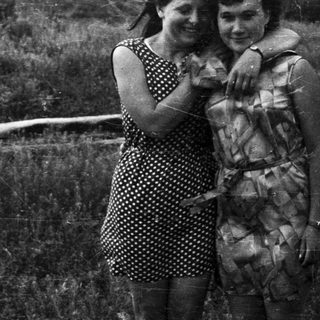 Two women embrace in a field with a log.