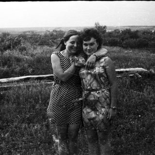 Two women embrace in a field with a log.