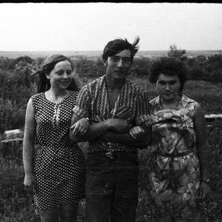 Three people stand in a field, looking directly at the camera.
