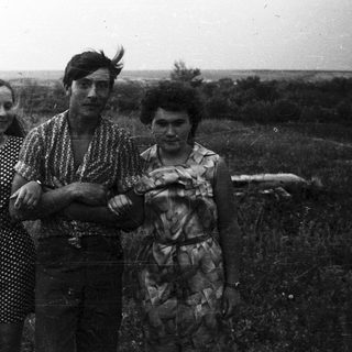 Three people stand in a field, looking directly at the camera.