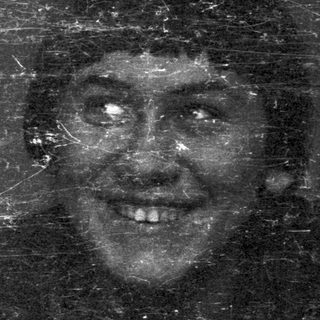 Man with a hat, smiling, visible through a scratched window.