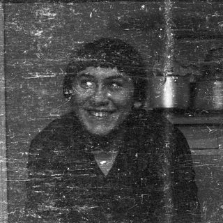Man with a hat, smiling, visible through a scratched window.
