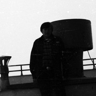 Man stands near industrial equipment, viewed in black and white.