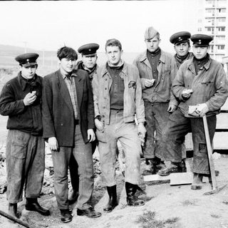 Group of men in uniforms standing near military vehicle.