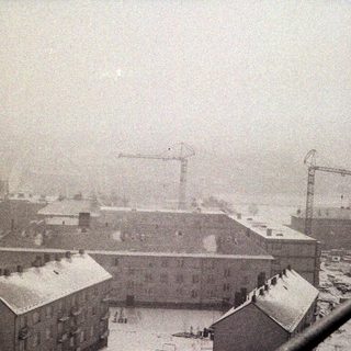 Snow-covered buildings and cranes under a heavy, overcast sky.