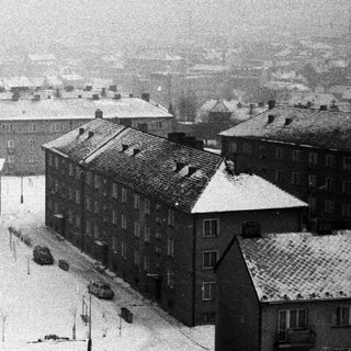 Snow covers rooftops and streets in a densely populated area.